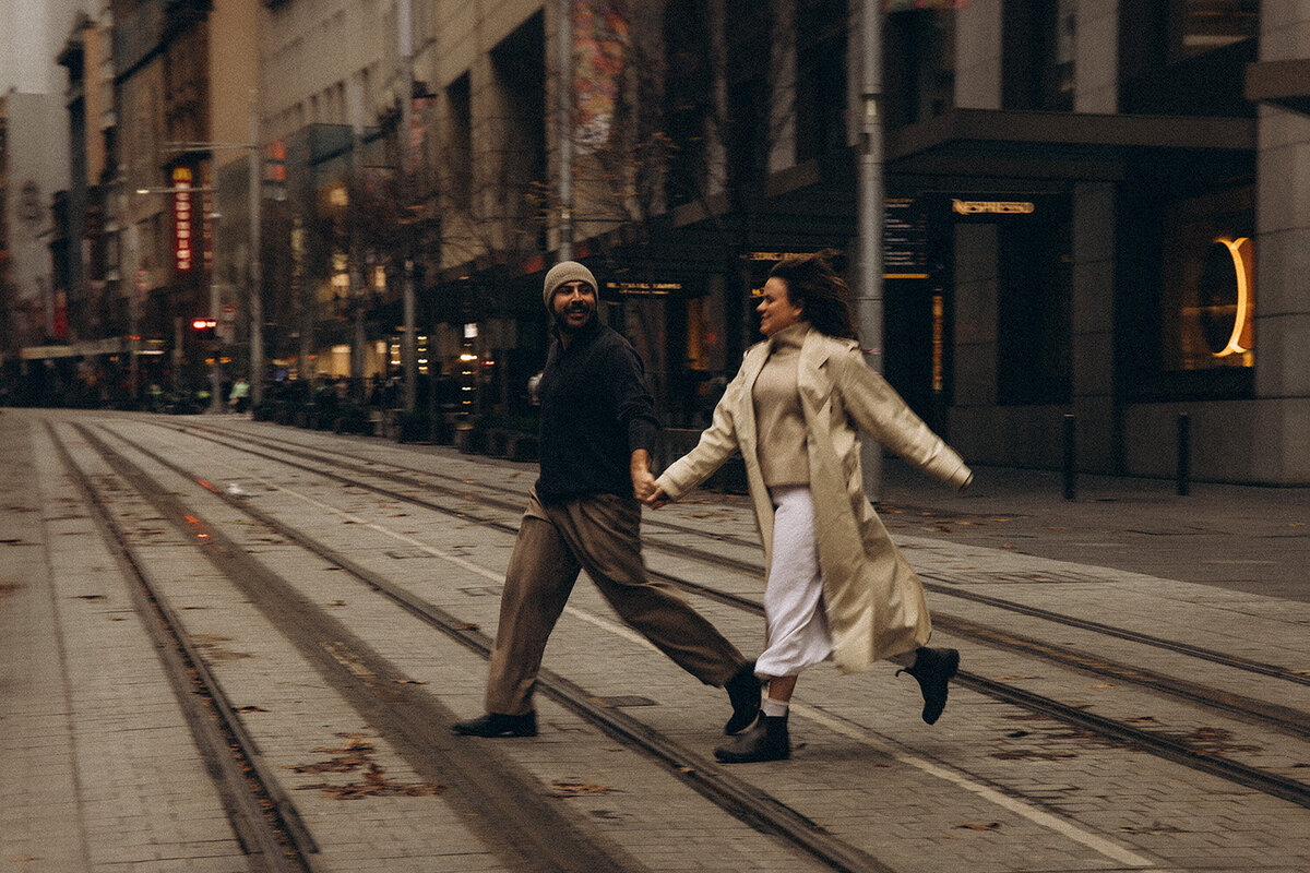 A couple running hand-in-hand through the city streets at dusk, captured by Nicci K Photography — couples photographer Sunshine Coast.