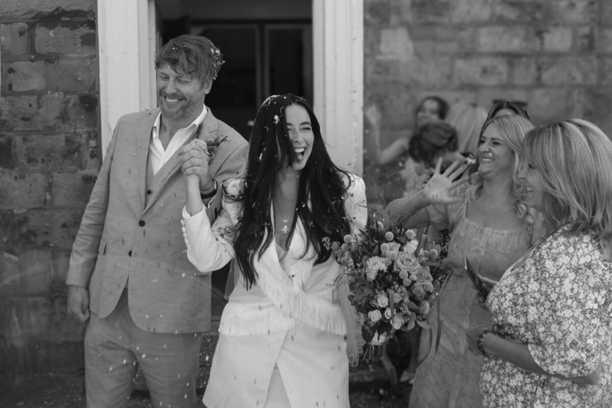 Wedding photographer captures the moment a couple walk out of their ceremony hand in hand whilst friends and family celebrate with confetti.