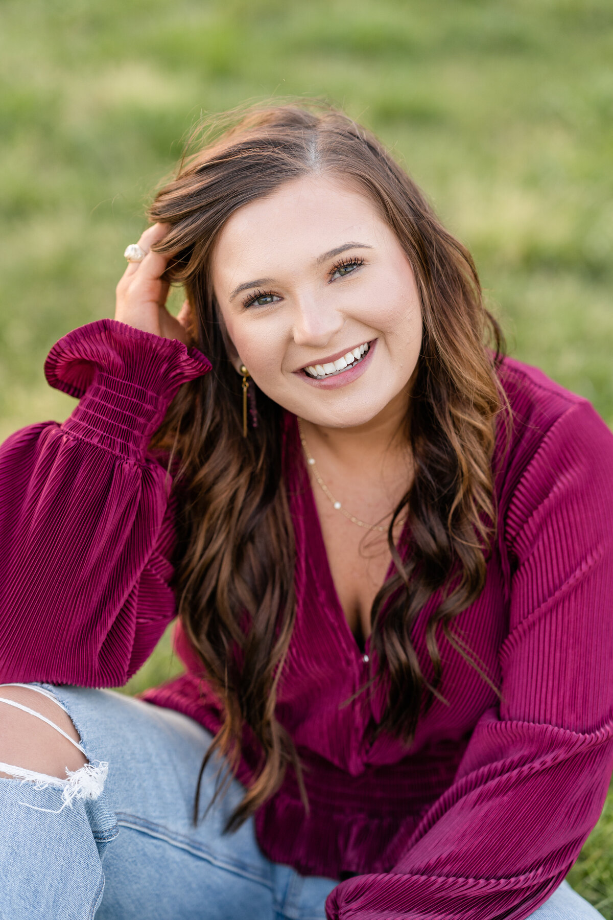 Texas A&M senior girl sitting on the ground and leaning on hand while wearing maroon shirt and jeans