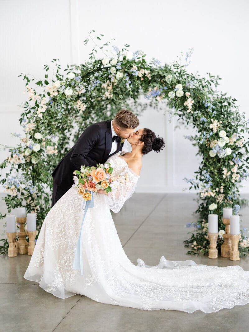 Bride and groom in front of floral arch kissing by wedding planners chicago