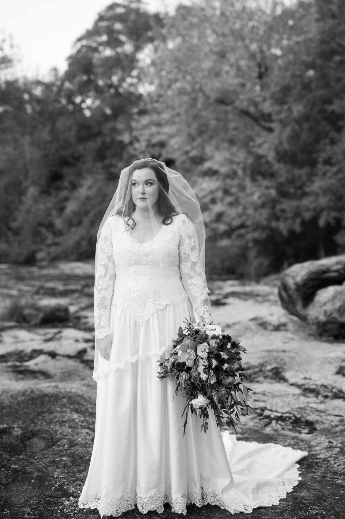 A bride with a veil over her head and a bouquet in one hand