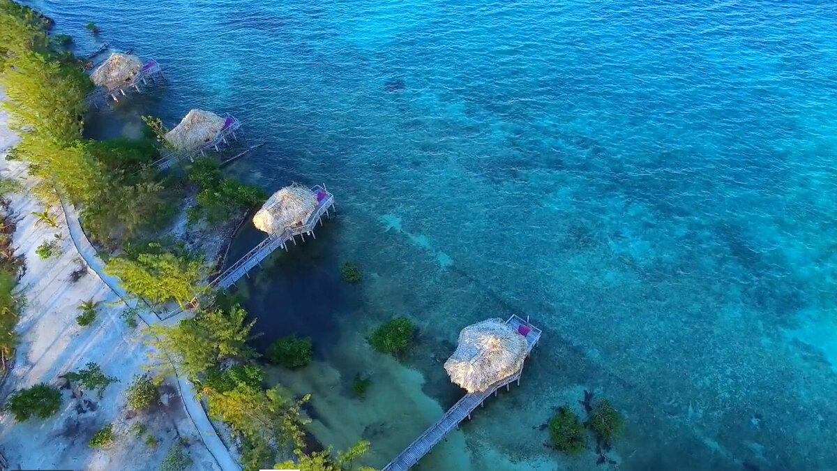 This is an overhead aerial photo of Thatch Caye in Belize showing blue waters and bungalows