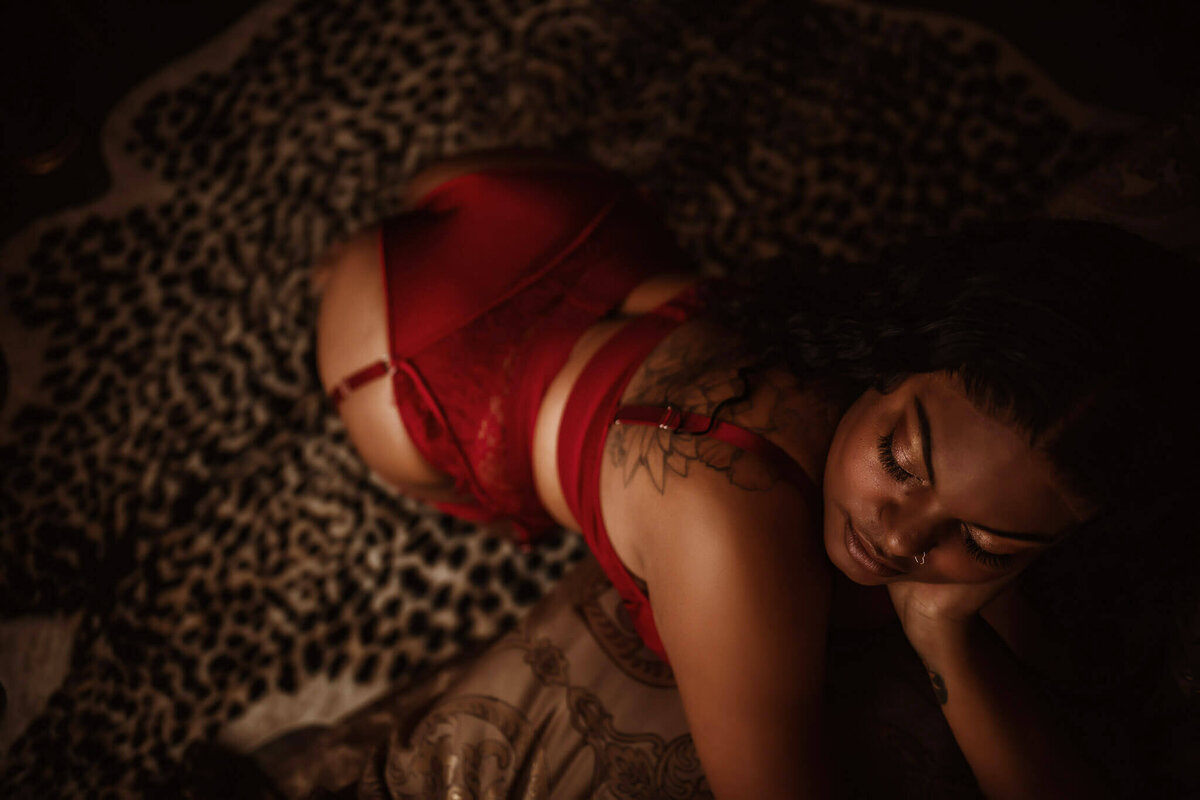 Woman in red lingerie leaning on a bed in a boudoir studio near Fort Worth