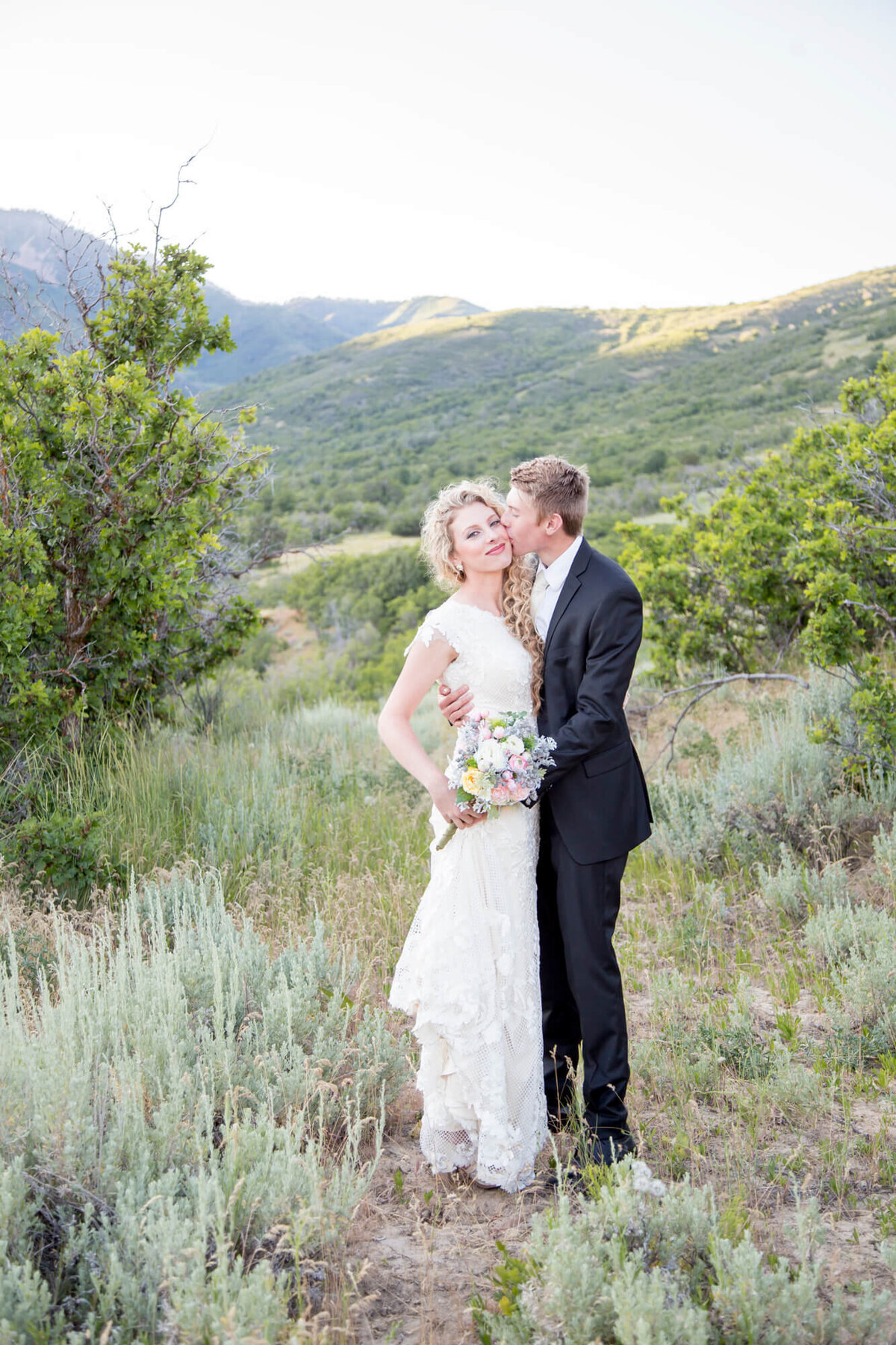 a groom kissing a bride in the mountains