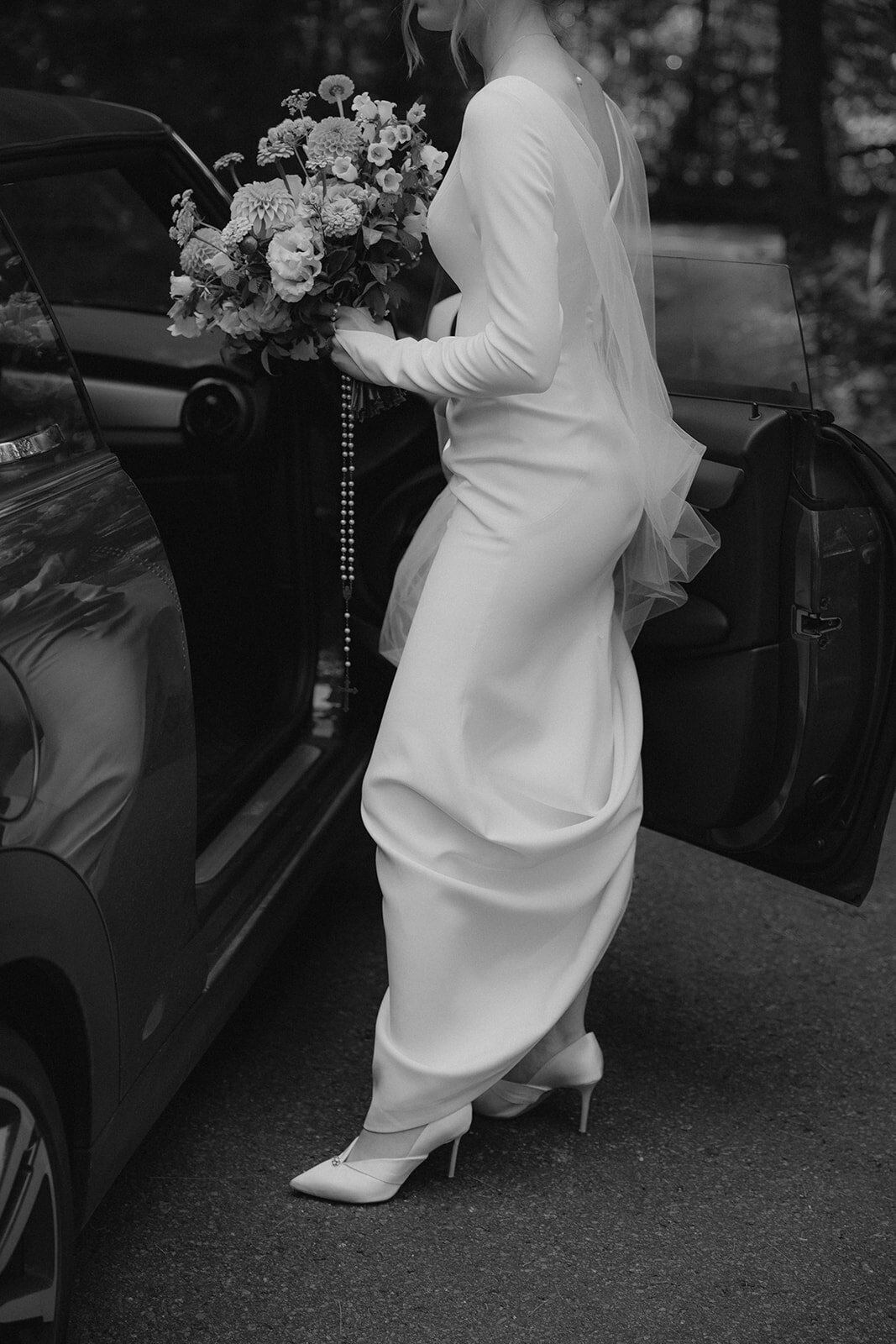 A bride holds a large bouquet as she enters a car at a Montreal wedding. 