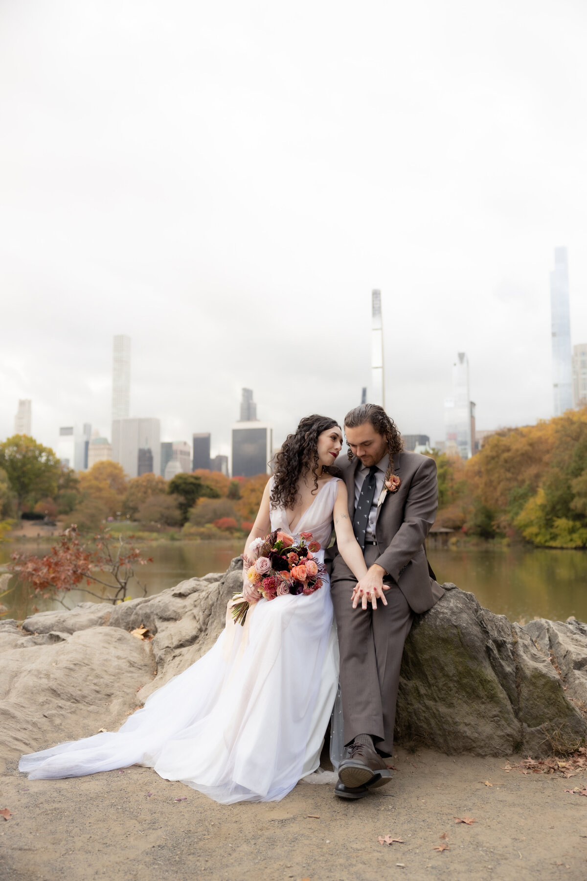 The couple standing close together surrounded by Central Park’s glowing fall foliage.