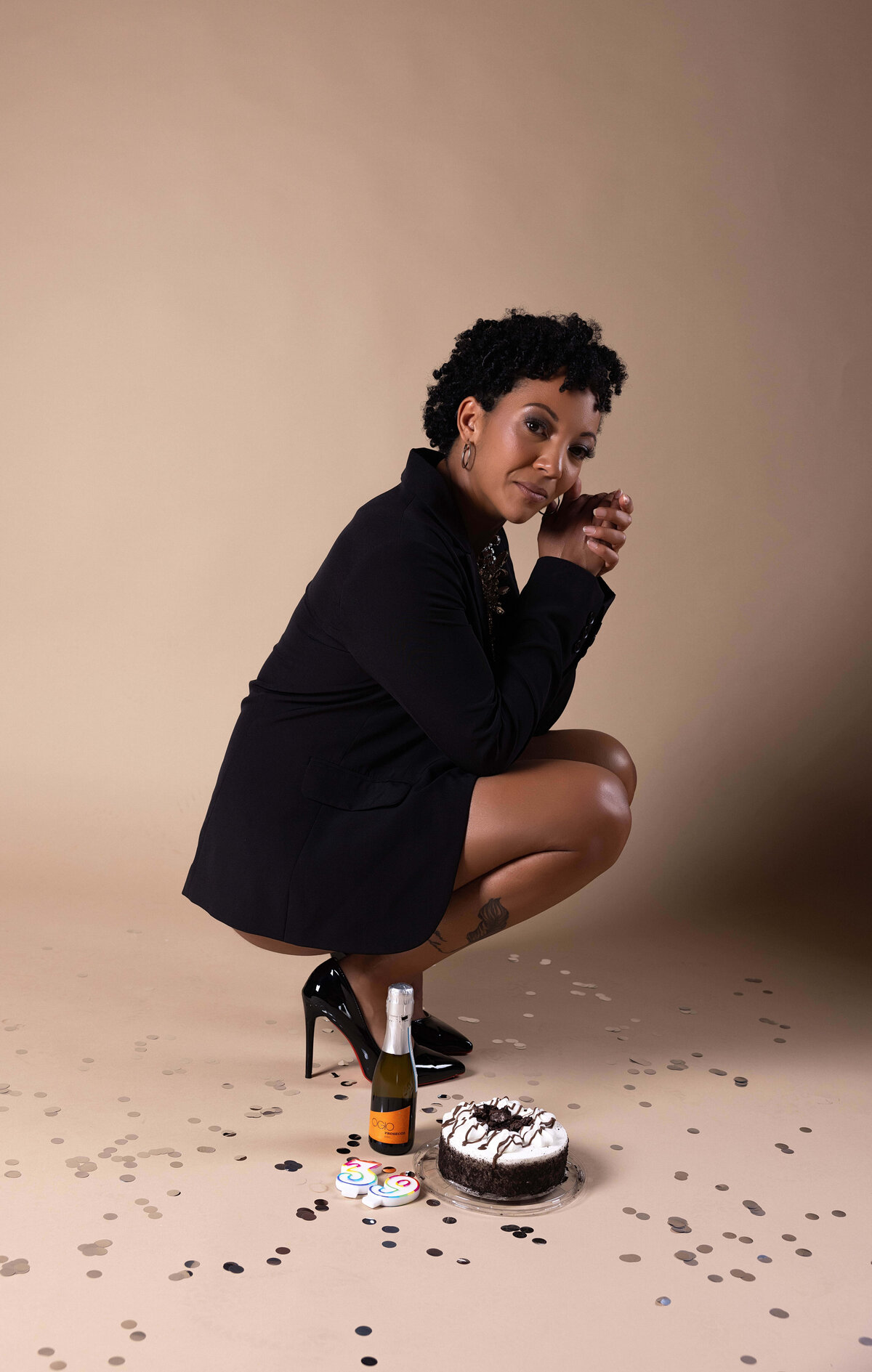 woman crouching in heels next to birthday cake and champagne in birthday session with reva davis photography