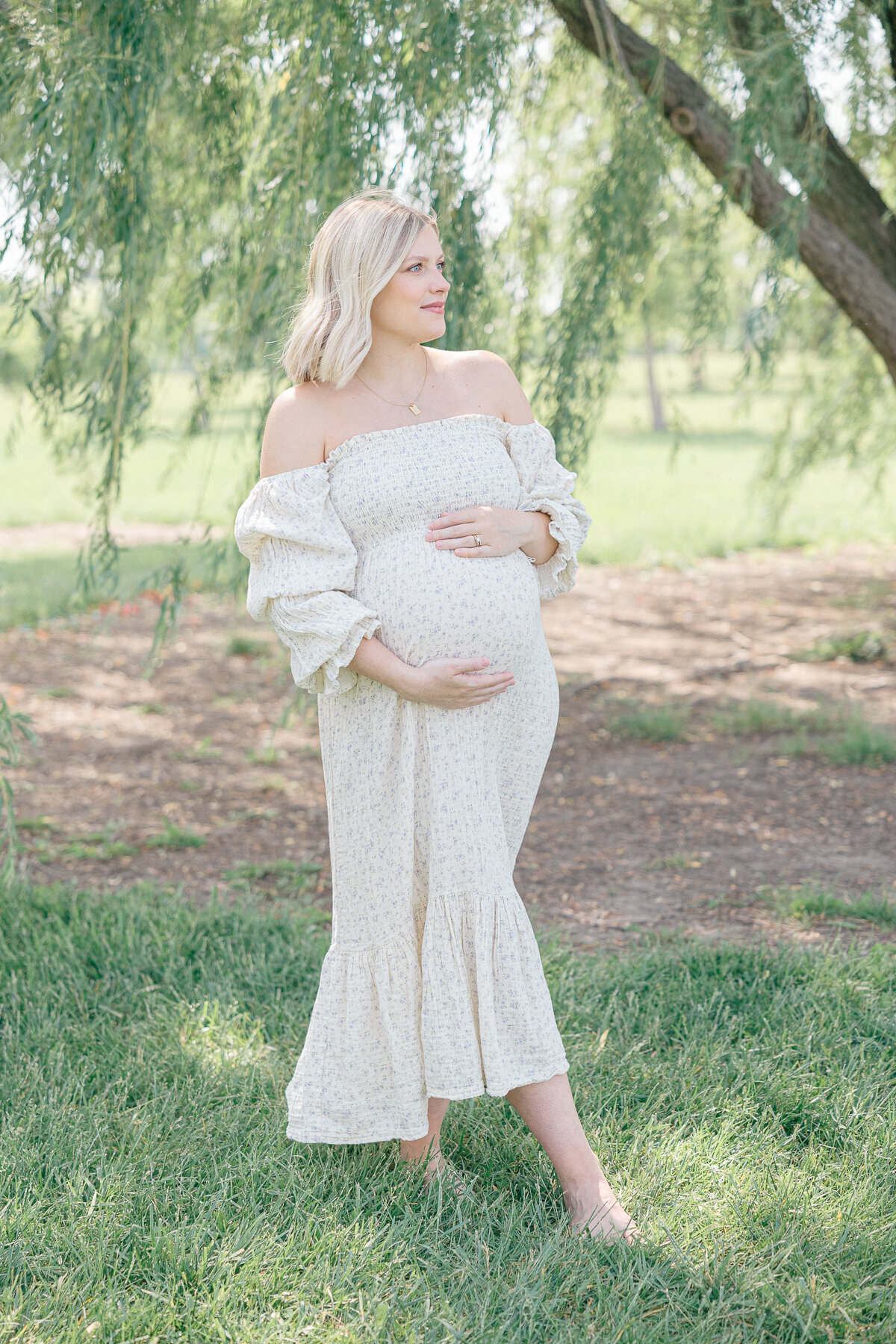 A pregnant mother holds her belly and looks off in the distance at her outdoor Indianapolis maternity photography session.
