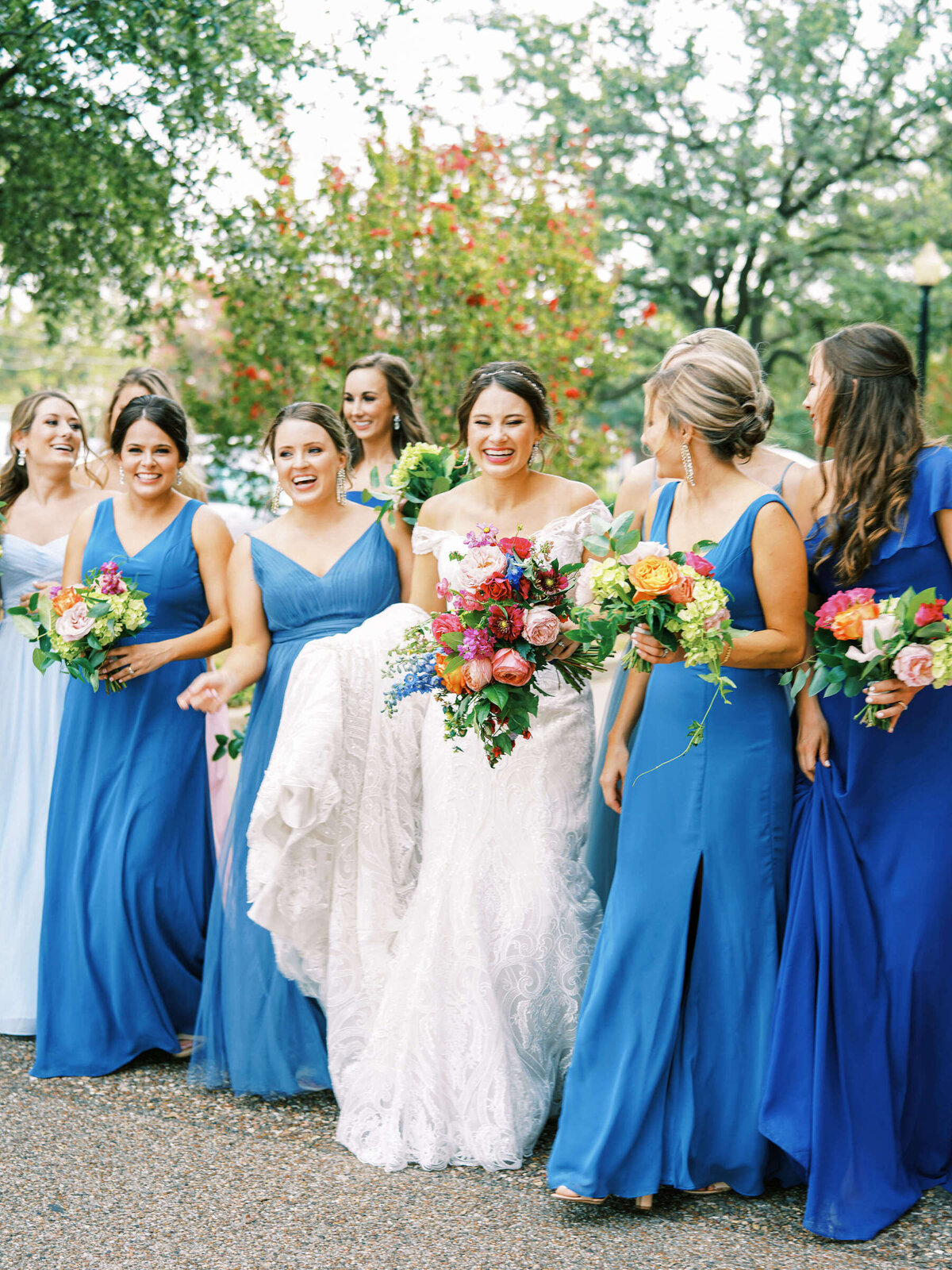 Bridal party in blue bridesmaid dresses walk with bride at summer wedding in Fort Worth Texas
