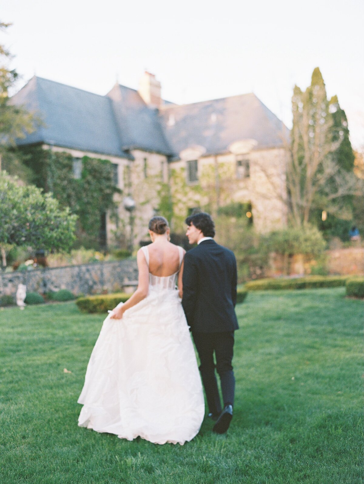 wedding couple walking toward stone mansion together