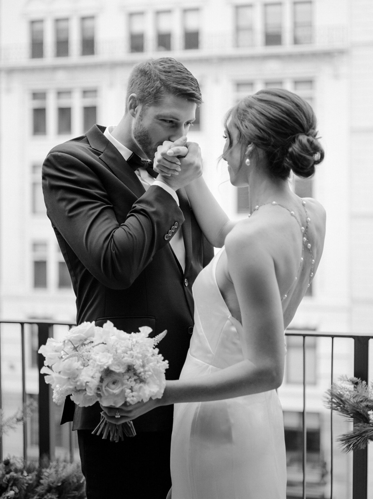 groom kisses bride's hand, backless wedding dress, pearl detail