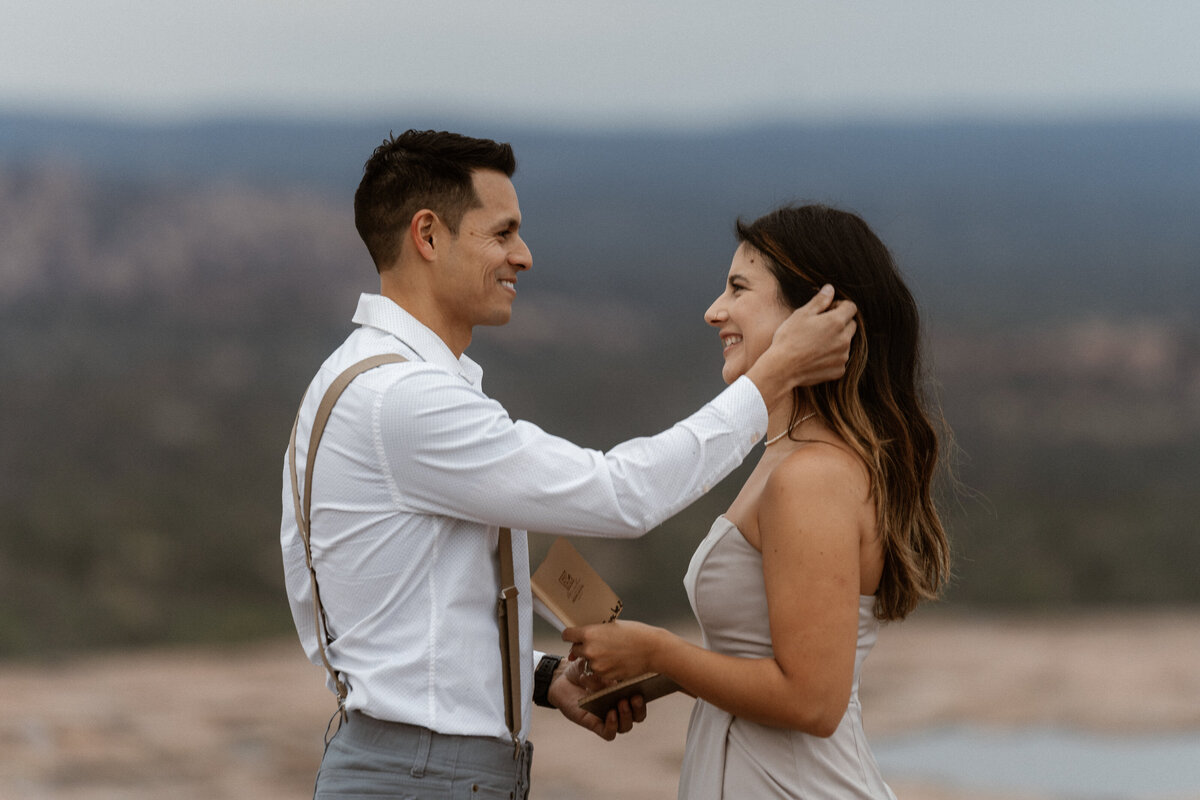 Groom intimately tucks bride's hair behind her ear during their vow renewal at Enchanted Rock with their two young children.