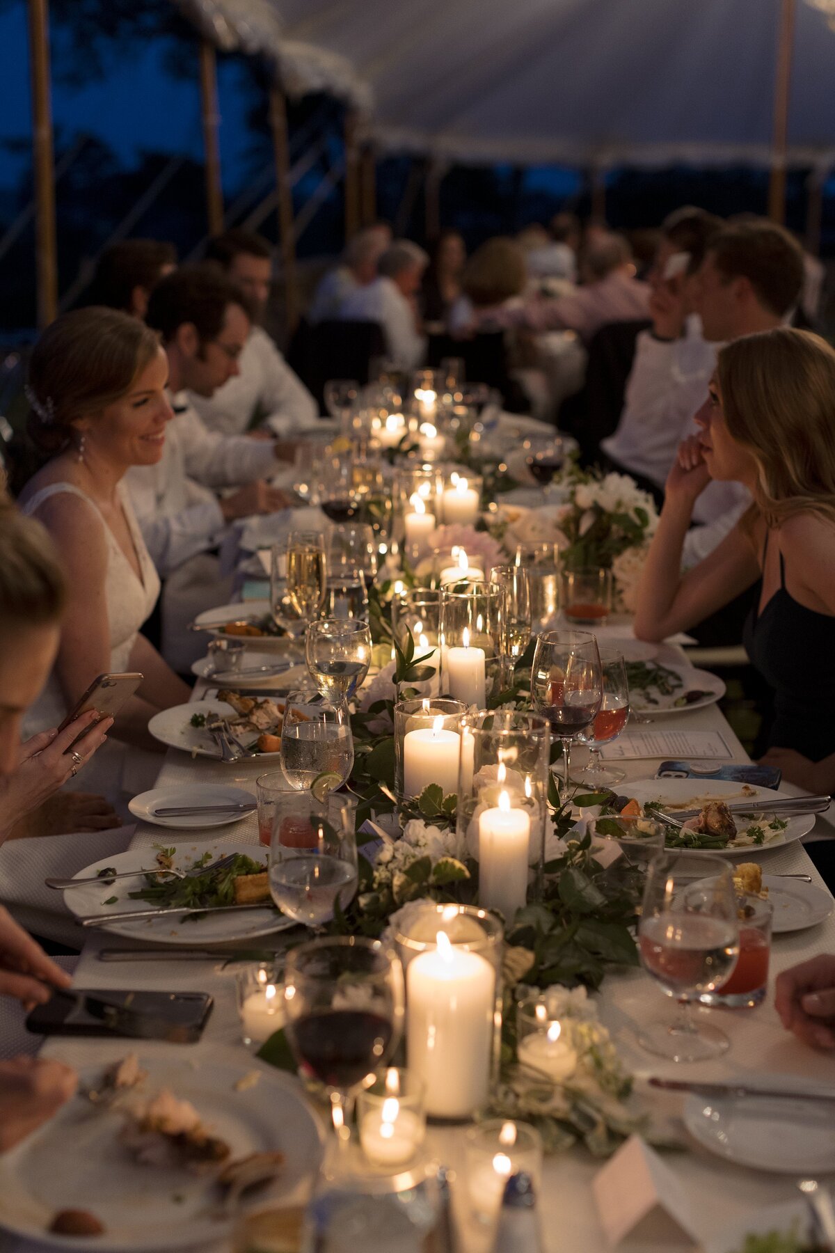 Wedding guests chat over table lit with candles during wedding reception at Crane Estate.