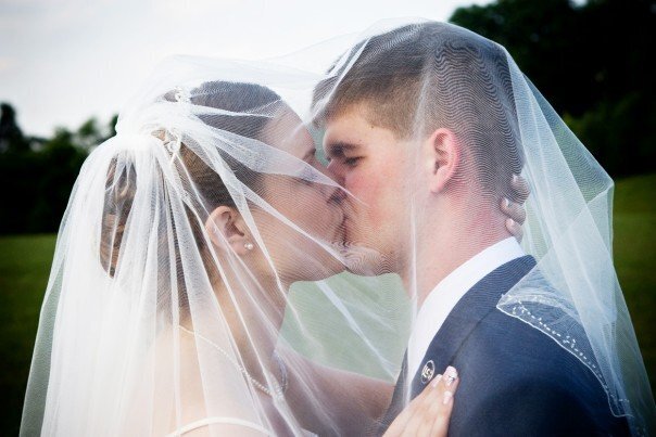 My husband and I kissing under my veil at our wedding.