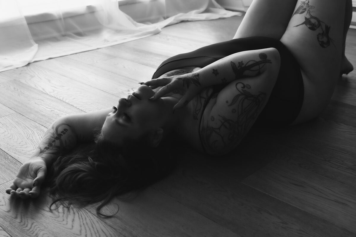 Tattoe woman posing on the floor for her boudoir black and white themed boudoir photoshoot.