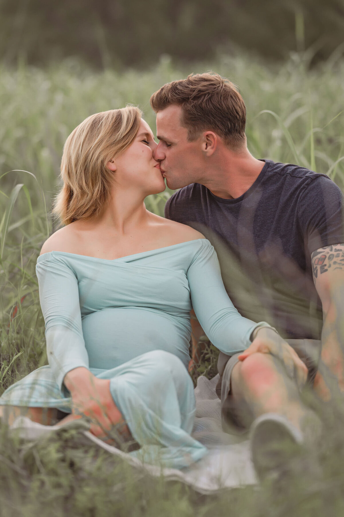 Young expecting couple kisses in a field of grass during maternity pictures with Cassey Golden Photography.