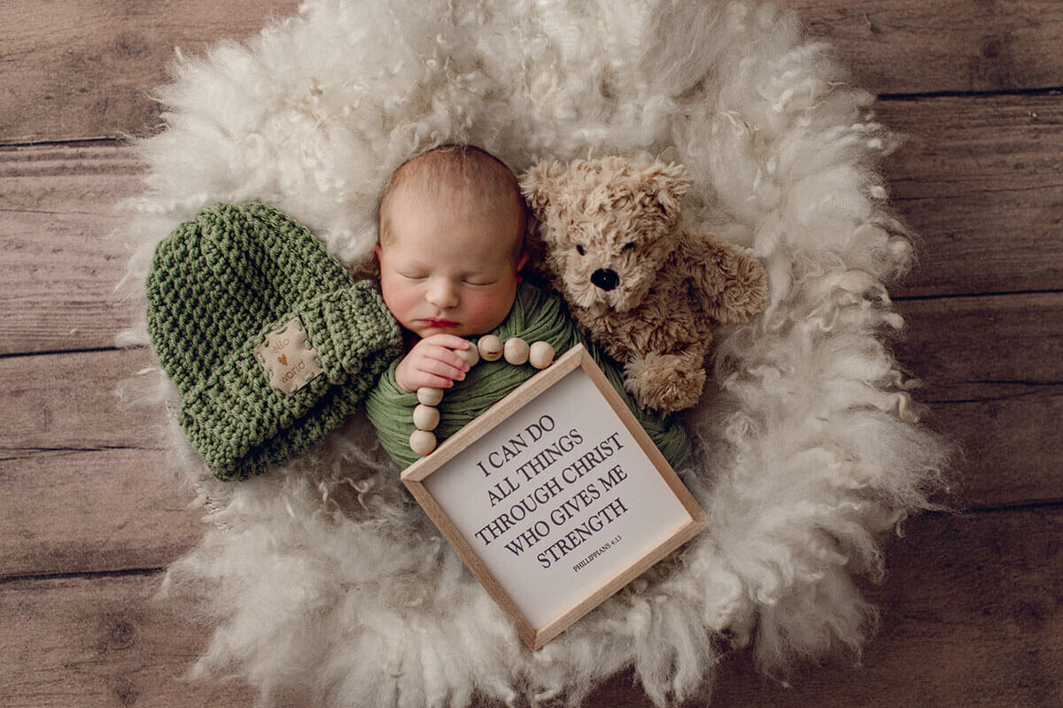 Rainbow baby cradled in green, peacefully holding a sign honoring his big brother in heaven.