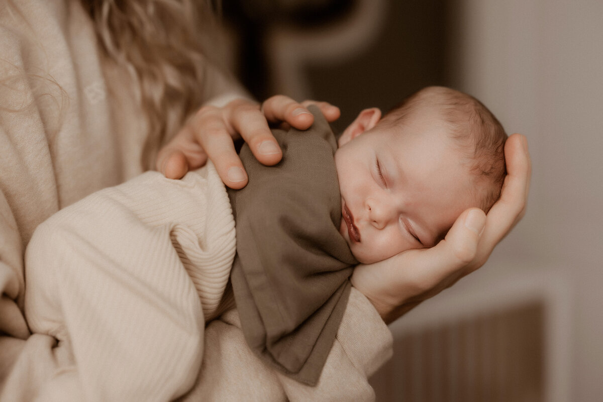 newborn baby boy lays on dad's arm in nursery