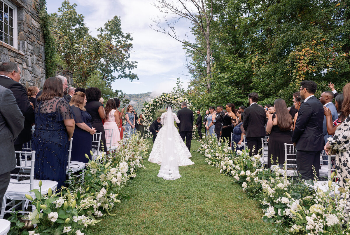Bride walking down a floral-lined aisle during the outdoor ceremony at Castle Ladyhawke.