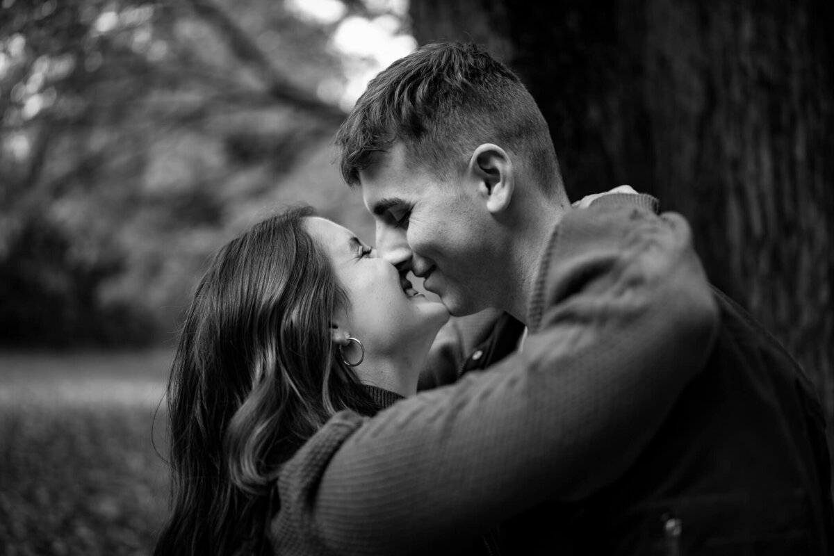 Black and White Pittsburgh engagement photos  of a couple holding each other  and smiling in front of the woods at McConnell's Mill State Park, Portersville PA