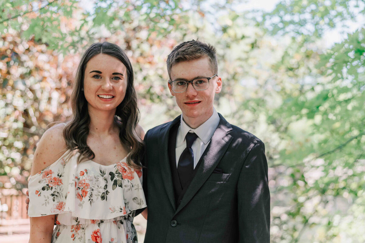Standing with his sister by some trees with pink flowers. 
