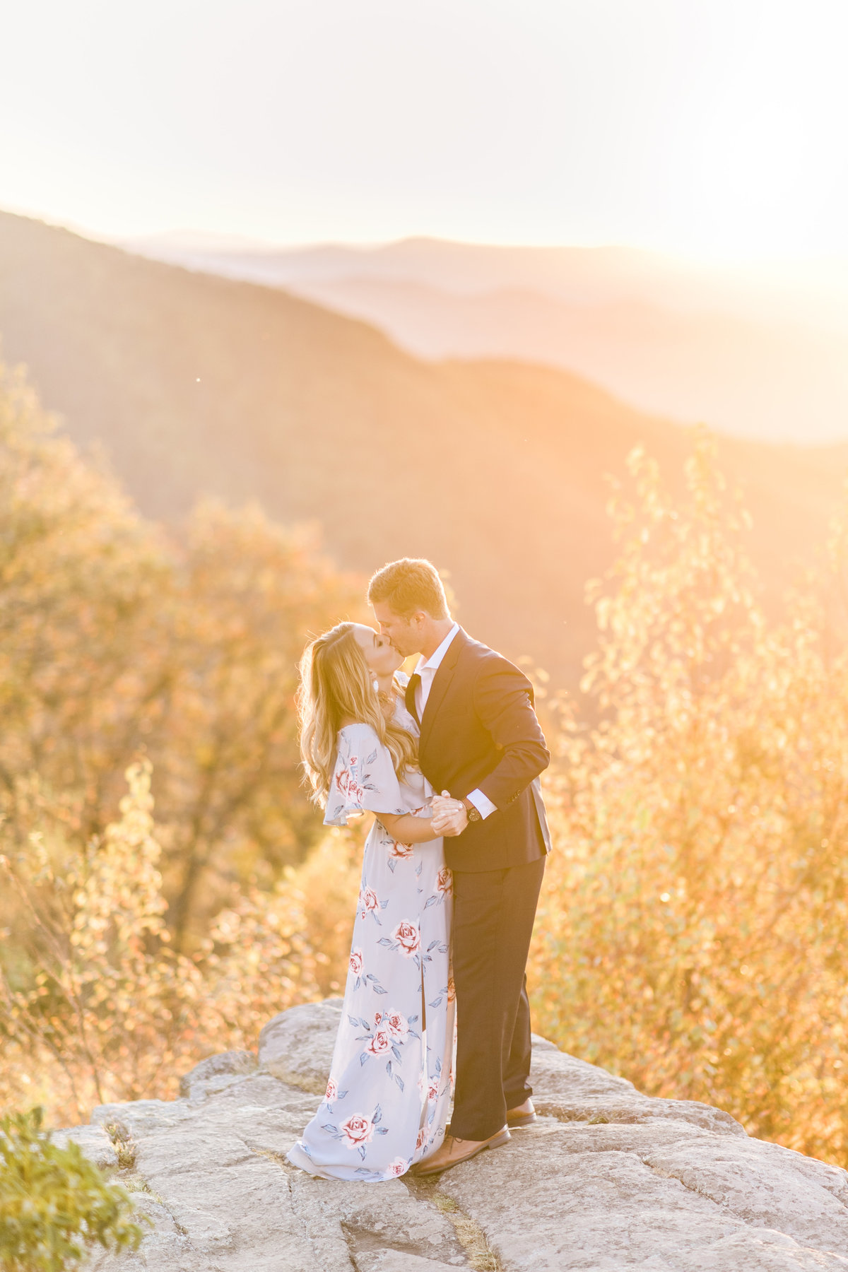 Well dressed couple kissing on a mountain at sunset.