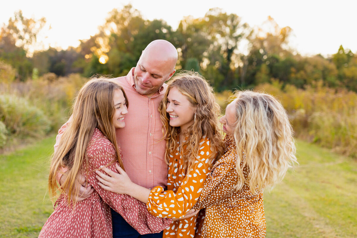 Family of four cuddled together in a hug in a large field