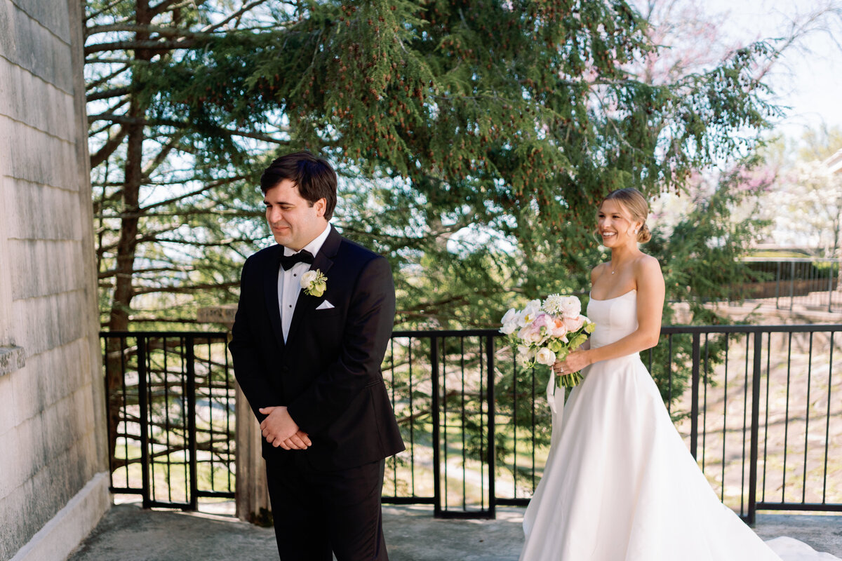 Bride walking up to the groom from behind, smiling and holding her bouquet during their first look at Burritt on the Mountain in Huntsville, Alabama, photographed by Perry Hancock.