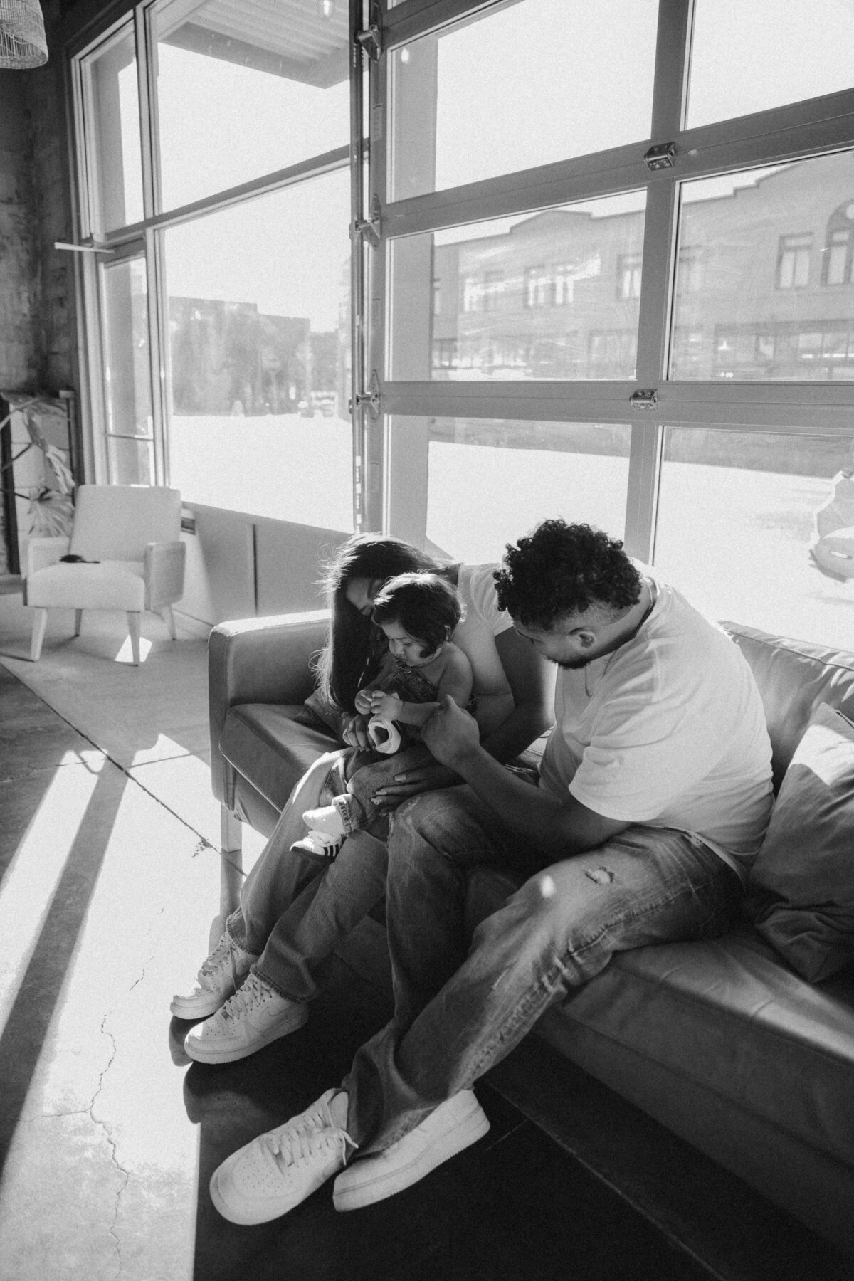 Black and White Family Photo Cuddling Baby on Couch in Natural Light Studio