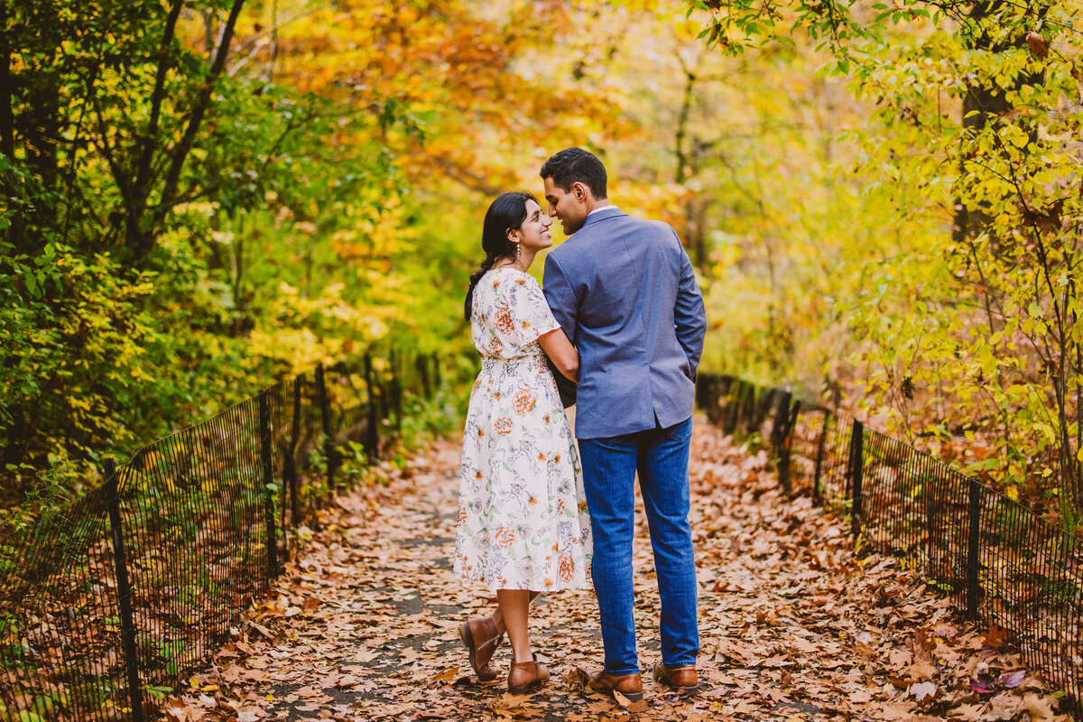 An engaged couple share a moment on a leafy walkway in the fall in a forest in central park near glenspan arch