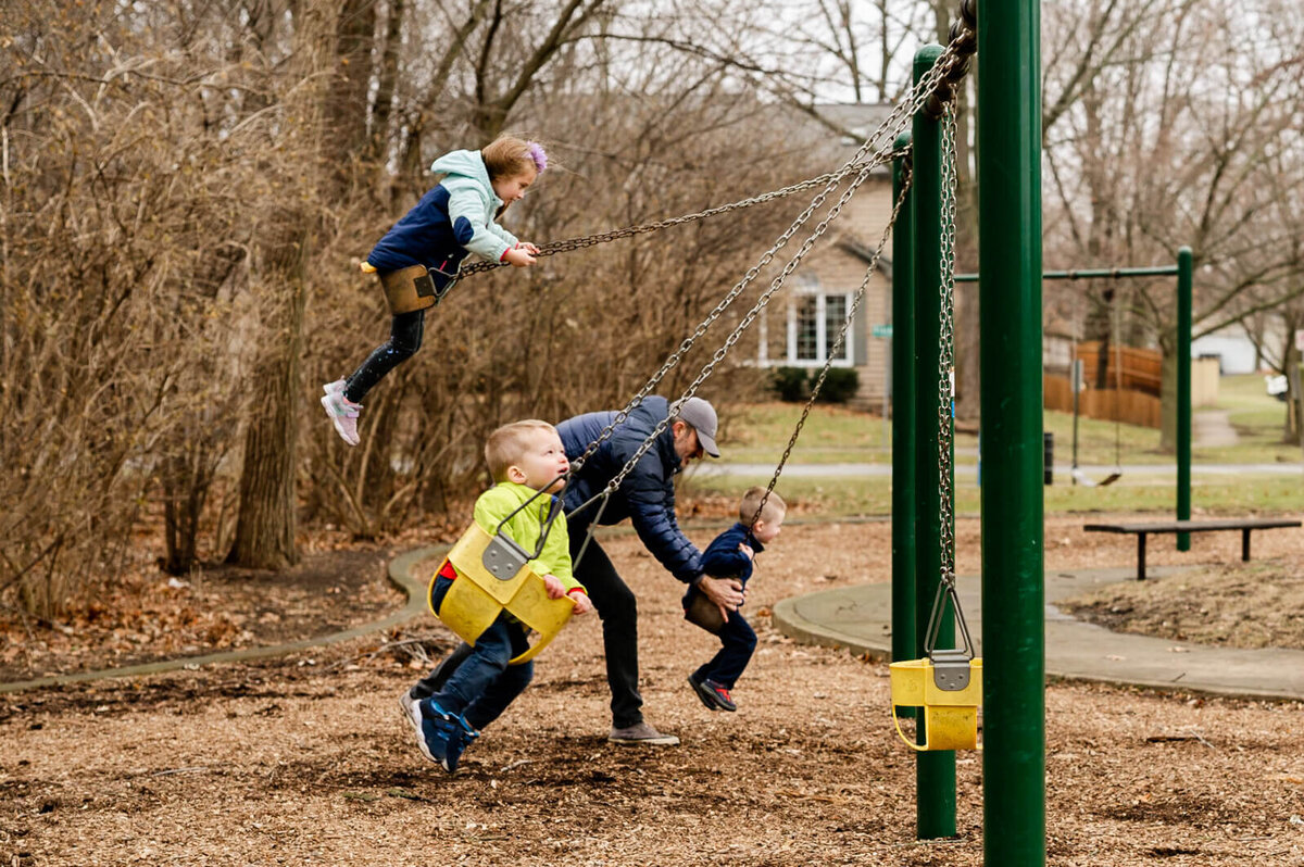 Father pushing multiple children at the same time on a swing set near Naperville, IL.