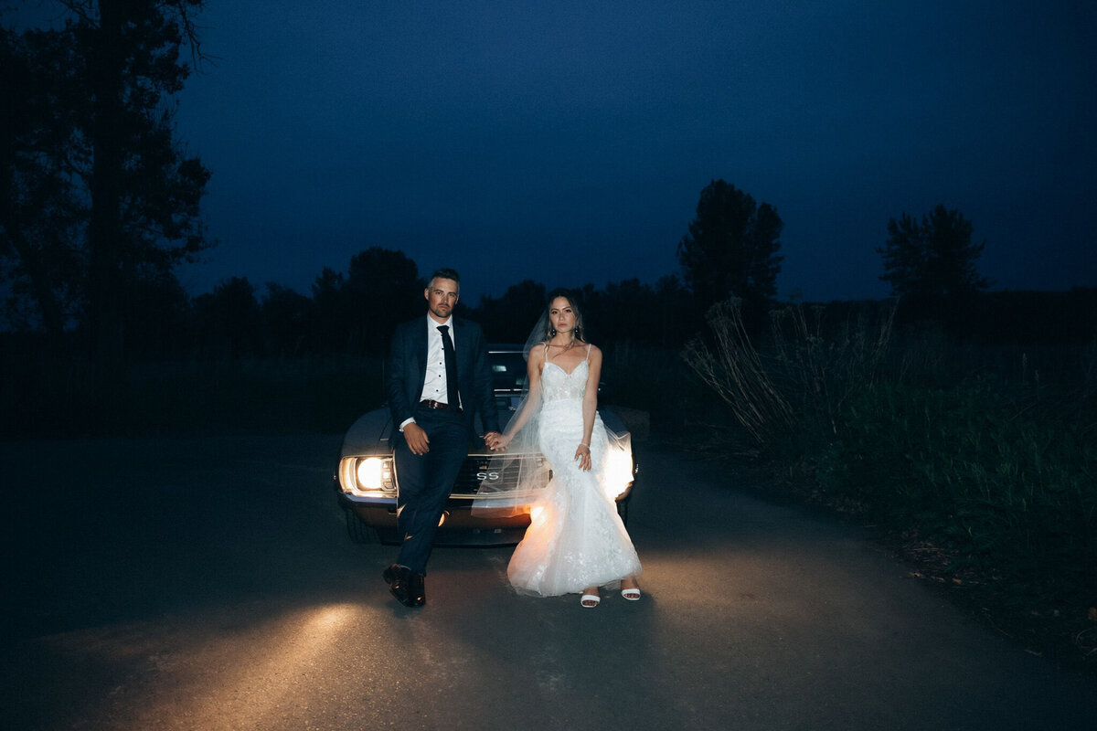 Bride and groom sitting on vintage car at dusk captured by Victoria Pattemore, adventurous and authentic wedding photographer in Calgary, Alberta. Featured on the Bronte Bride Vendor Guide.