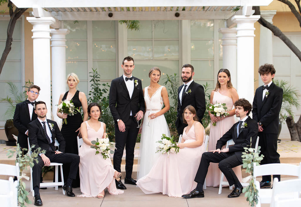 A wedding couple posing with their wedding parties sitting and standing around them.