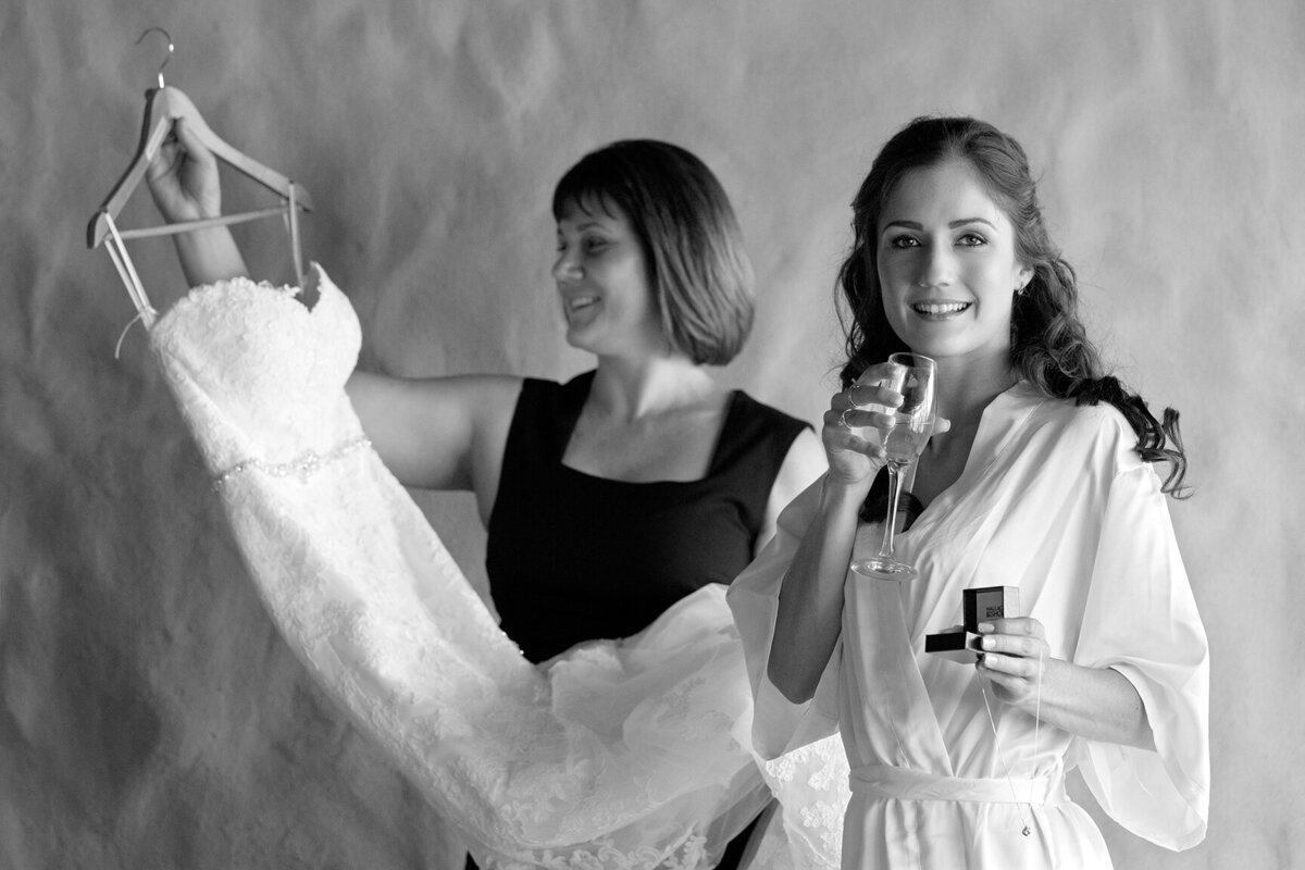 Exquisite moments unfold as the bride celebrates with champagne, her mother gently holding the wedding dress. Explore heartfelt wedding photography capturing the essence of joy, elegance, and cherished memories, beautifully frozen in time.