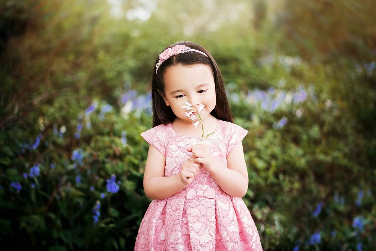3 year old girl smelling a flower in a pink dress