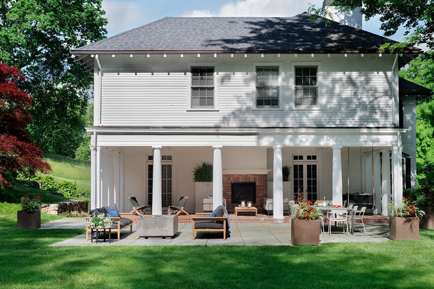 Overall view of the historic house with a new bluestone patio next to the brick porch, featuring seating, lounging, and dining spaces with mature gardens. As seen on Boston Home Magazine's Instagram.