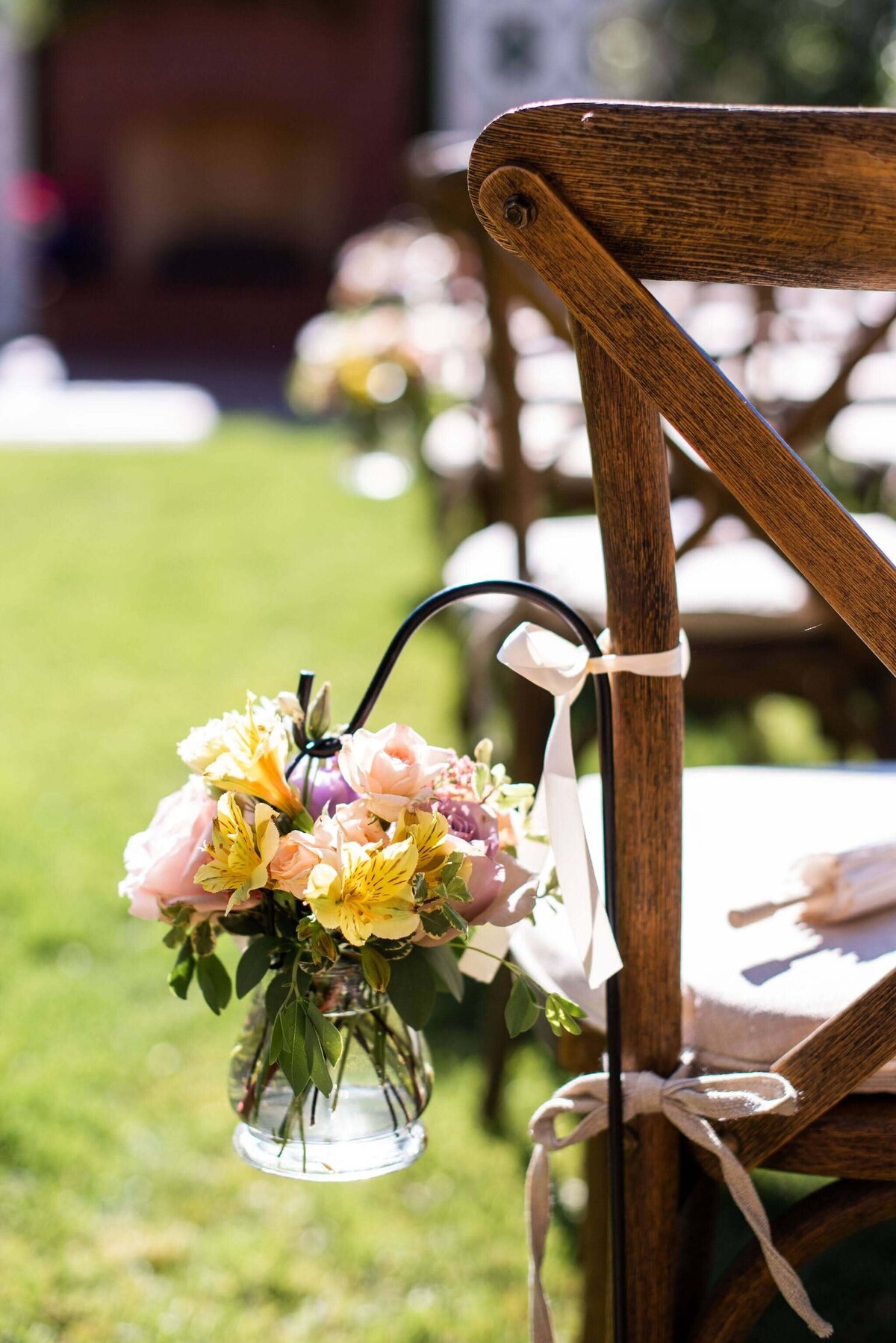 Small floral arrangement hangs from a chair along the aisle of a wedding ceremony.
