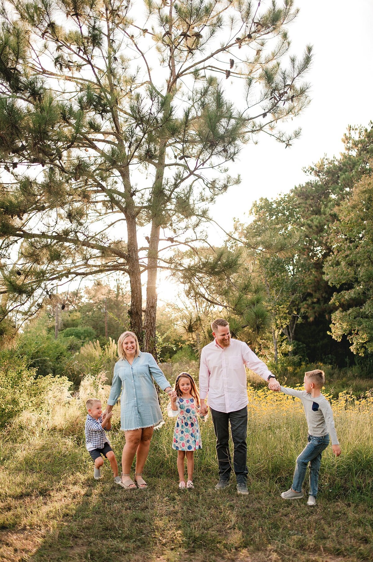 Family of five standing and holding hands standing in a field by Cypress Family Photographer