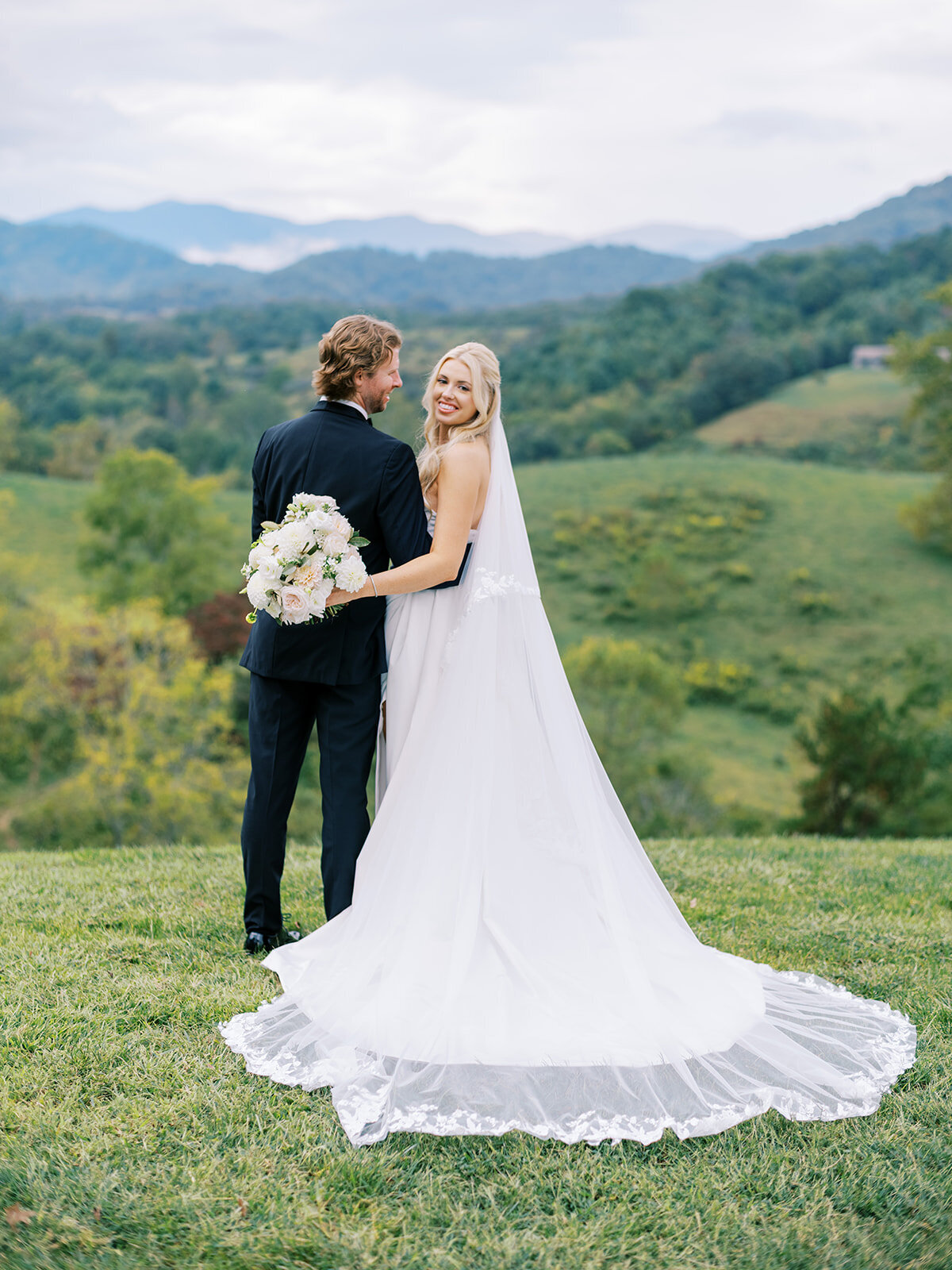 Bride and groom pose on a hill overlooking Blue Ridge Mountain views at The Waynesville Inn & Golf Club wedding in Waynesville, NC.
