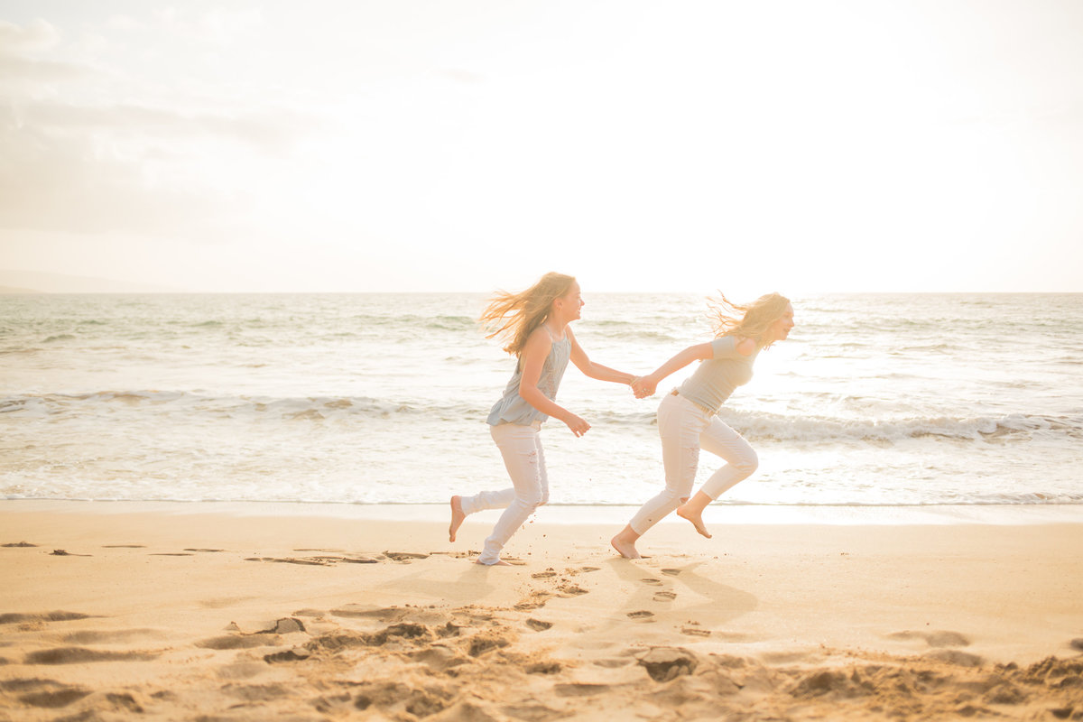 Two girls running in the sand, hand and hand