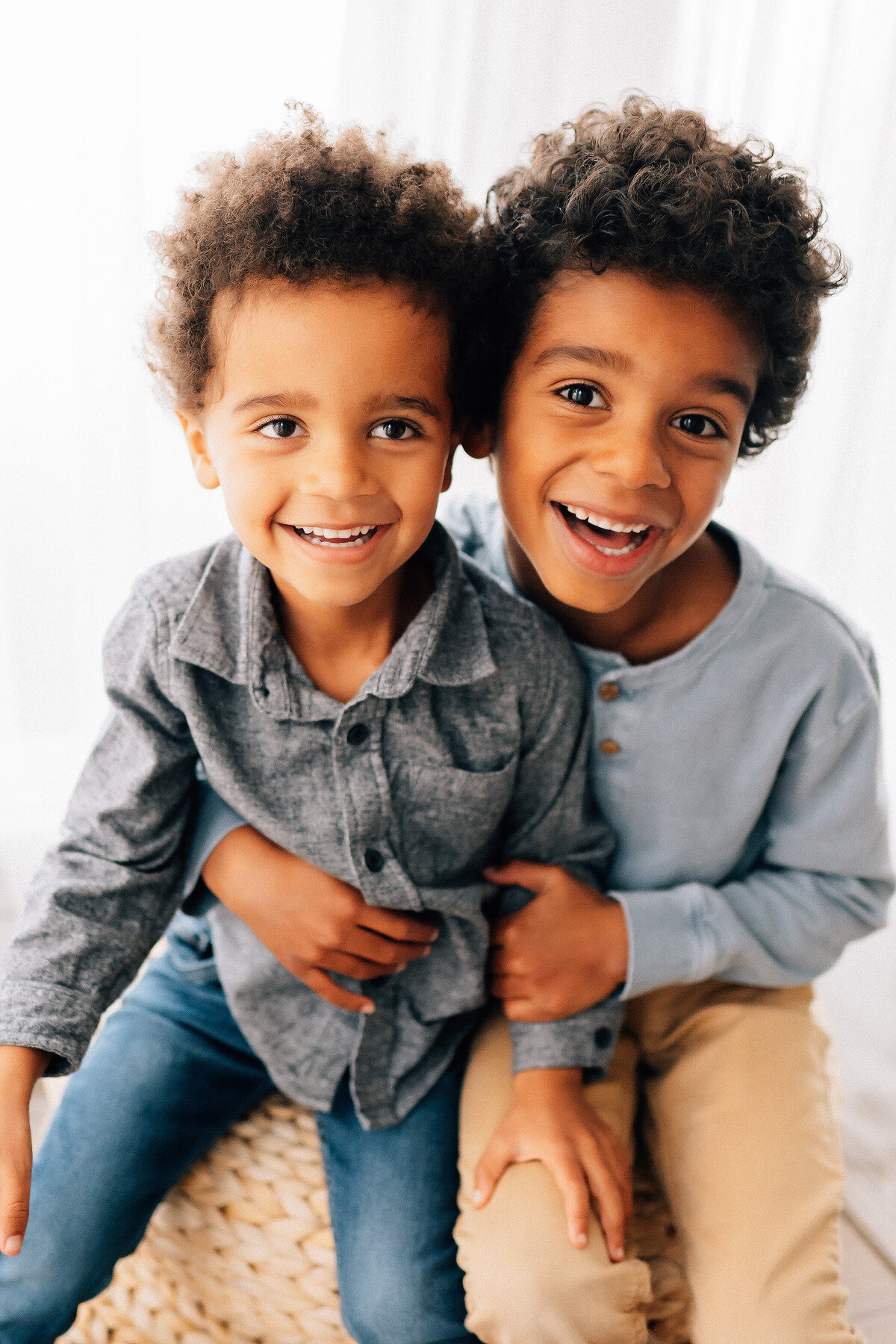 two brothers sitting together in front of a window looking at photographer 