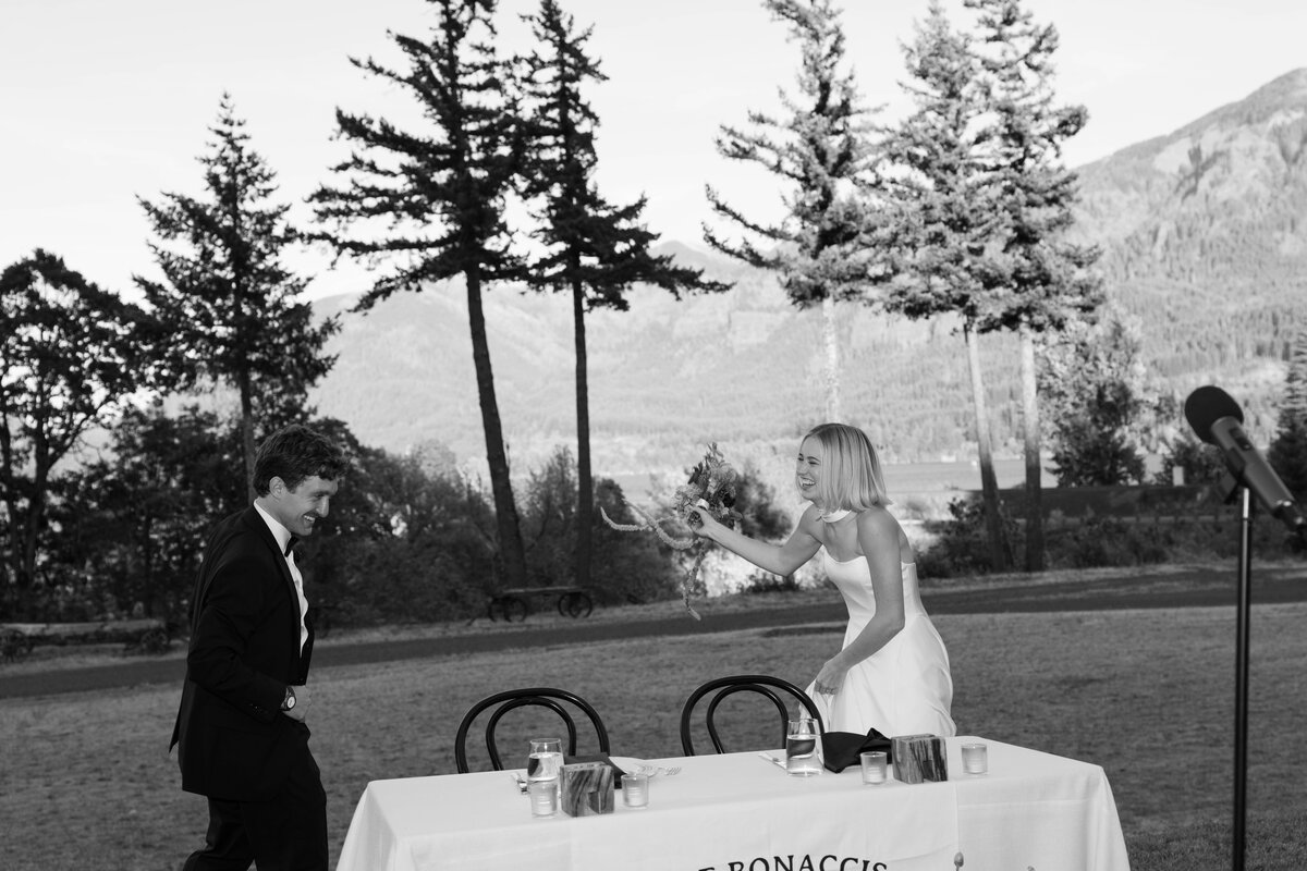 Bride playfully tossing bouquet to groom during outdoor wedding reception