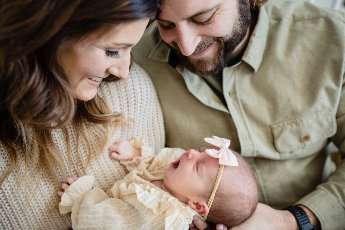 A close up of a mom and dad holding their newborn baby and gazing while smiling into her eyes.