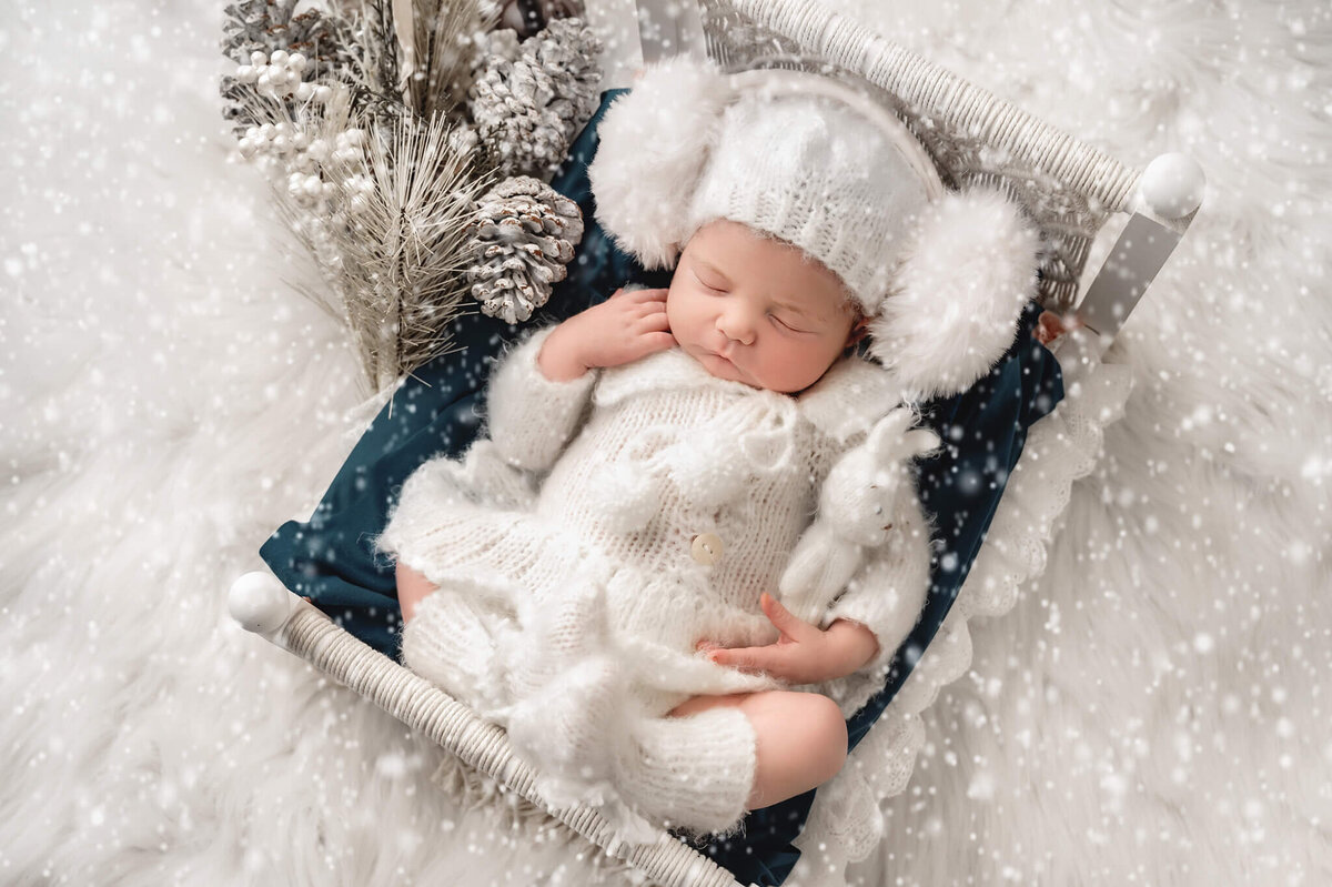 Newborn girl sleeping on a bed cozy in a white knit outfit in a winter scene at Toronto Newborn Photo shoot.