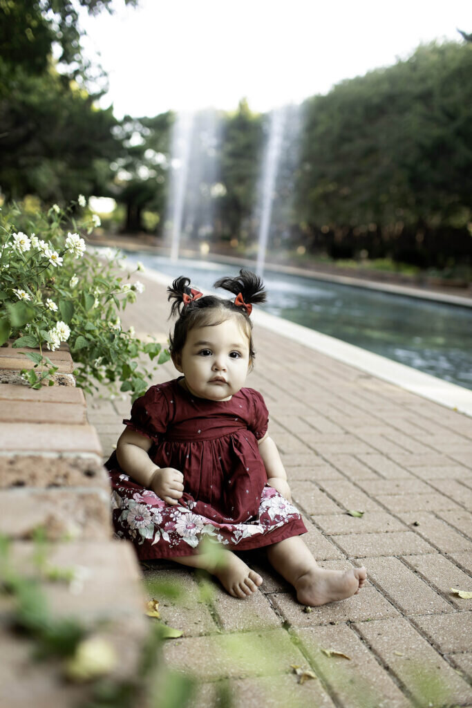 One-year-old girl wearing a simple dress, sitting on the floor and looking at the camera with a soft smile