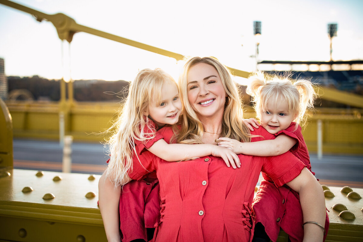 A mother and her two daughters Post on the bridge with the sunset glinting off of their golden hair as they embrace