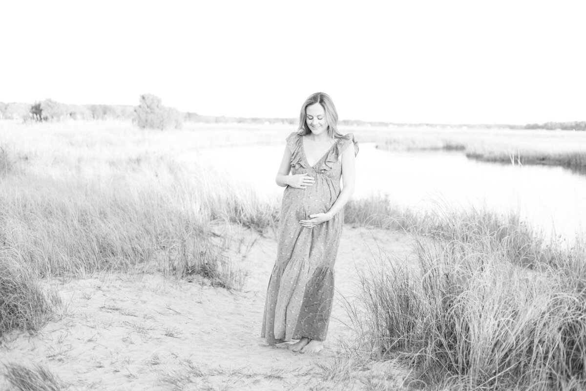 Black and White Virginia Beach Maternity Photo of a pregnant woman  smiling down while cradling her belly