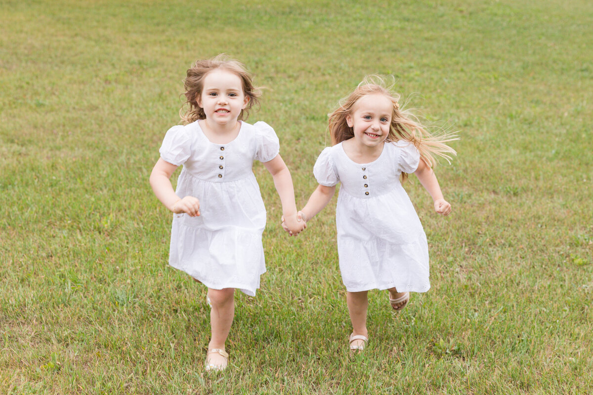 Two little girls are holding hands and running toward the camera while smiling