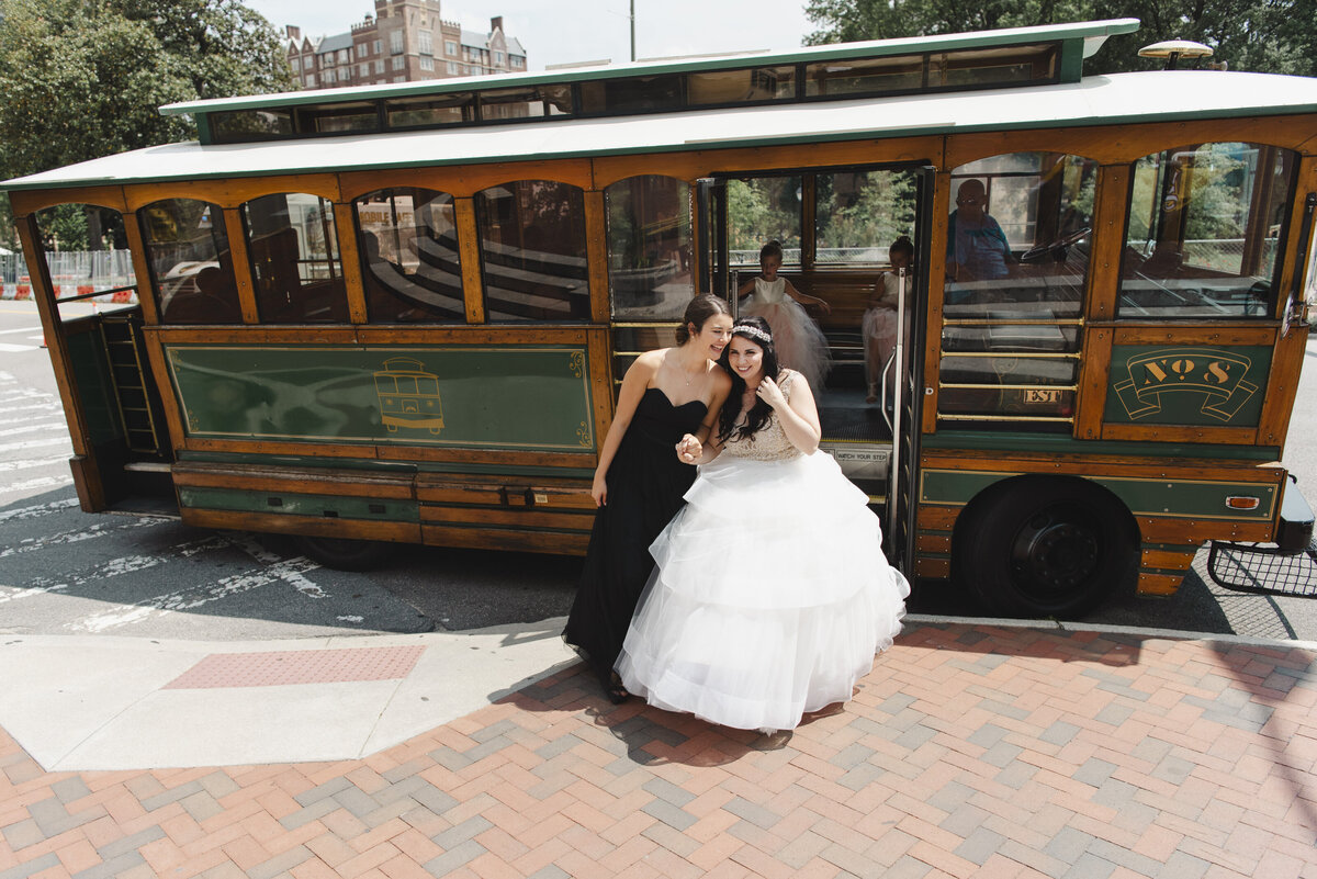 Two people stepping out of an old style bus while one is in a wedding dress 