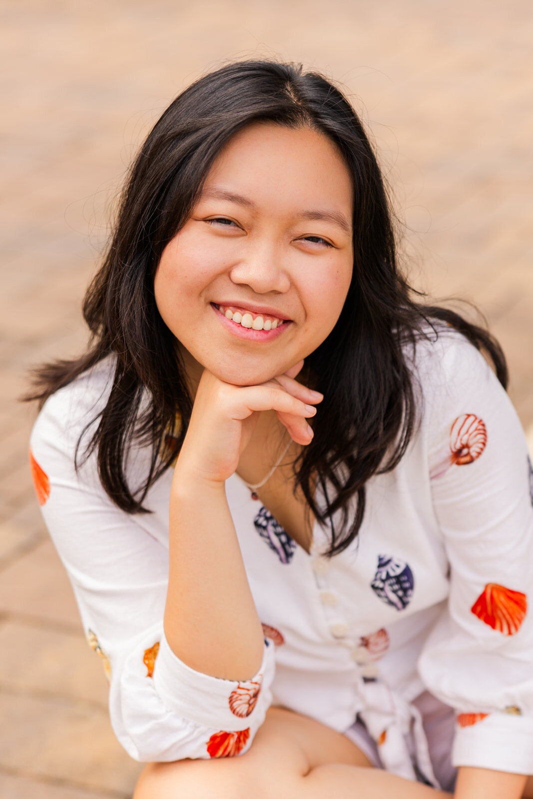 teenage girl sitting on the ground legs crossed resting her head on her hand during senior photoshoot in Sandy Spring with a city vibe